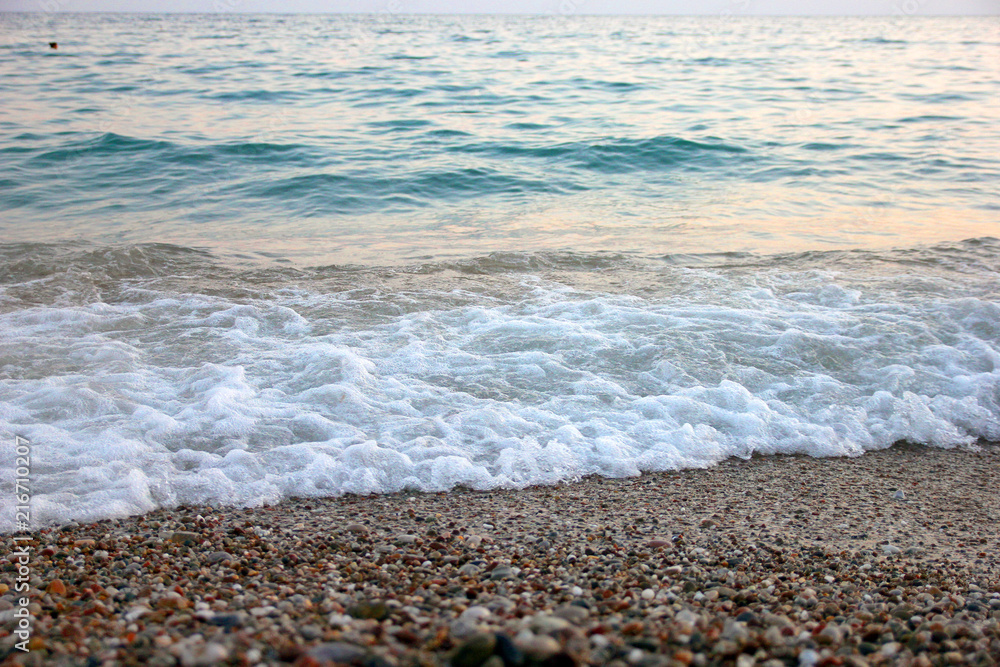 foam surf with blue sea waves on pebble beach of mediterranean sea on turkish coast in the evening