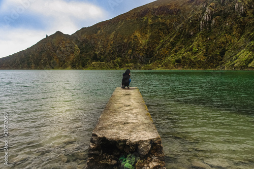 Happy person / young pretty girl admiring and taking a photograph on top of an old ancient pier / photo of the beautiful Lake Lagoon of Fire in Sao Miguel Azores, Portugal photo