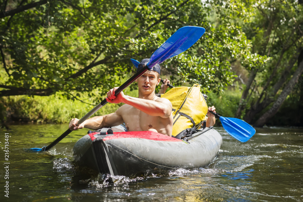 Kayaking on river. Athletic guys in canoe rowing with oars. Active recreation in nature. Water adventure. Rafting on river. Two friends in kayak with oars. Men are swimming along river in a kayak