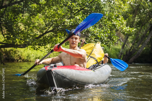 Obraz na płótnie Kayaking on river. Athletic guys in canoe rowing with oars. Active recreation in nature. Water adventure. Rafting on river. Two friends in kayak with oars. Men are swimming along river in a kayak w salonie