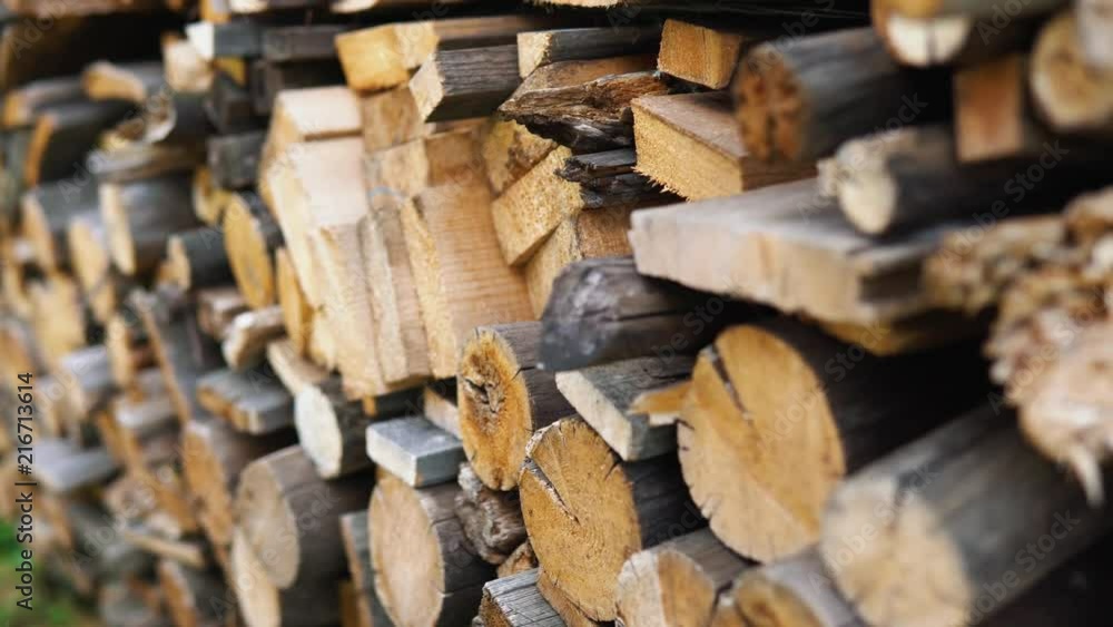 The chopped and sawn old trunks of trees is stacked in a large log woodpile in the yard. Stacked firewood prepared for the fireplace and stove, dolly shot. The chopped and sawn old trunks of trees is stacked in a large log woodpile in the yard. Stacked firewood prepared for the fireplace and stove, dolly shot.