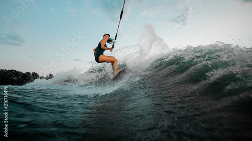 Young beautiful woman riding on the wakesurf holding a rope of a motorboat