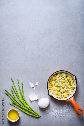 Healthy breakfast. Pan of fried scrumbled eggs with asparagus on grey background