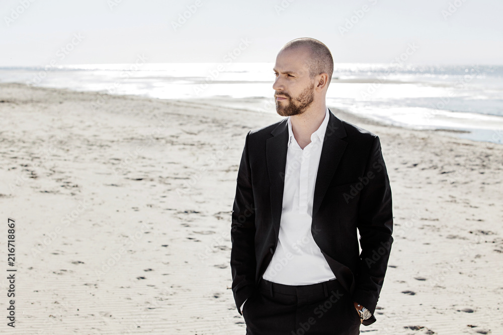 Confident young handsome man in classical suit on sandy beach looking away. Confident young handsome man in classical suit on sandy beach looking away.