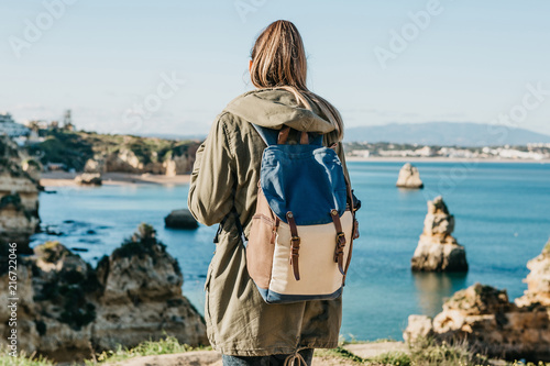 A tourist girl or a traveler with a backpack admiring the beautiful view of the Atlantic Ocean in Portugal.