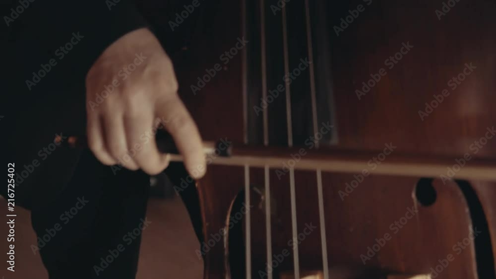 Camera moves from the face of a male cellist to his hands using a bow on a cello Camera moves from the face of a male cellist to his hands using a bow on a cello