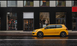 Yellow car is parked at asphalt road in the city center in the rain. Storefront