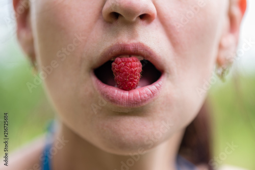 A girl is holding a raspberry berry in her mouth