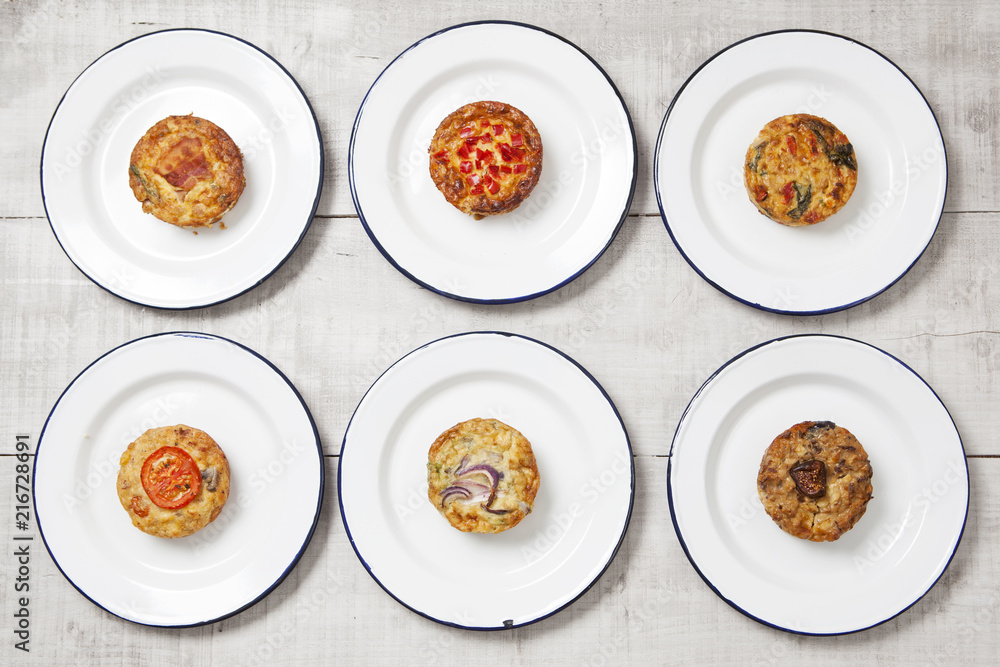 Individual quiches on white enamel plates on a light coloured tabletop Individual quiches on white enamel plates on a light coloured tabletop