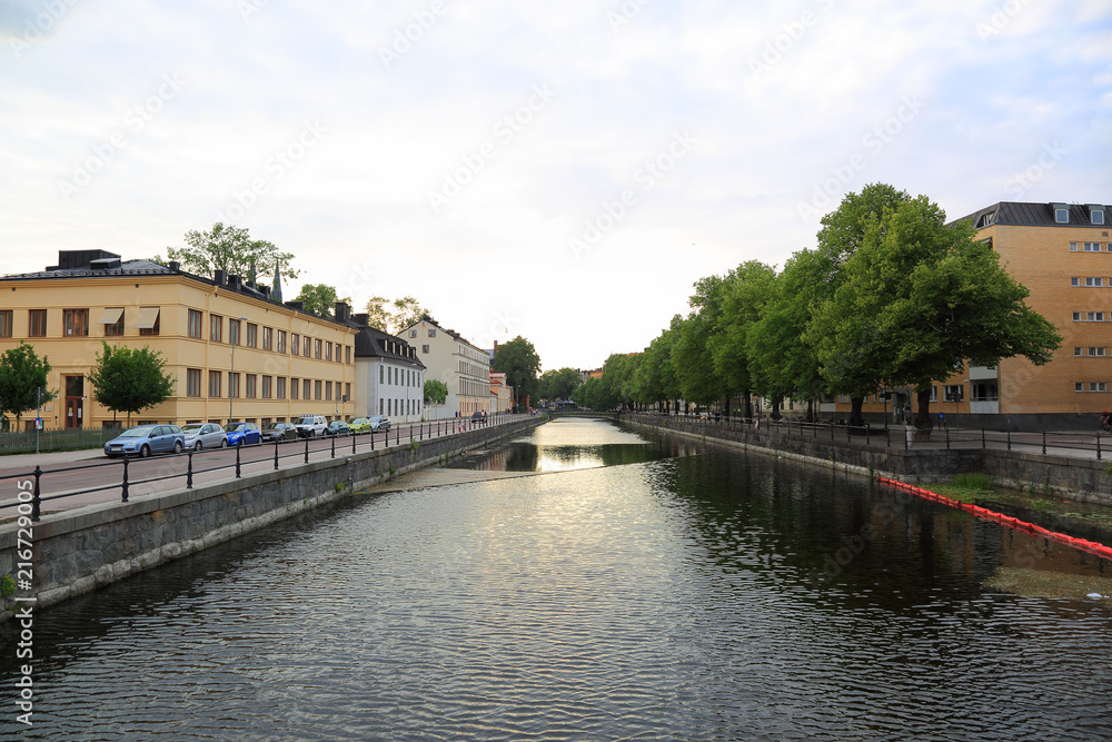 Beautiful landscape view of riverside, Uppsala, Sweden, Europe. Yellow buildings and green trees on blue sky background. 