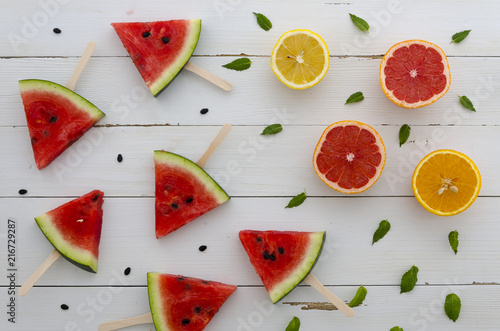 Fototapeta Naklejka Na Ścianę i Meble -  Juicy and fresh summer background with watermelon red slice popsicles arranged with cut citrus and mint leafs on a white rustic wood background. flatlay
