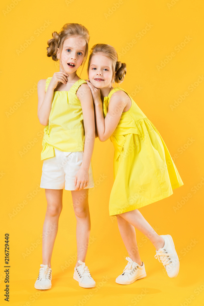 The girls of the twins stand together on a yellow background.