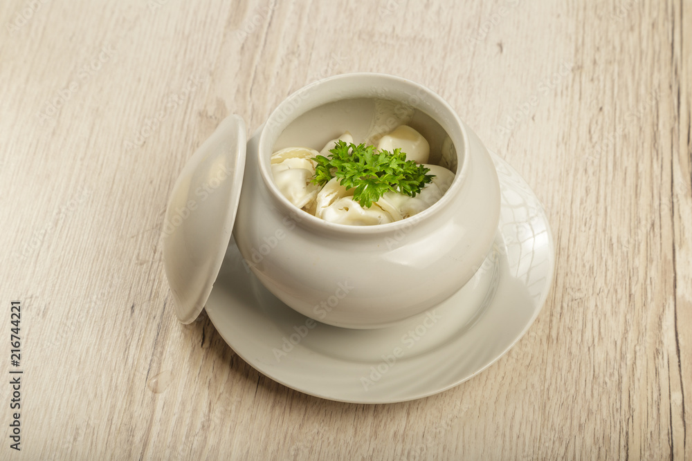 Dumplings in a white pot with sour cream and greens on a wooden background. Dumplings in a white pot with sour cream and greens on a wooden background.