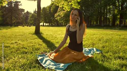 Front view of a female sitting towards camera talking during a phone call outdoors in the park. Slow motion shot. photo