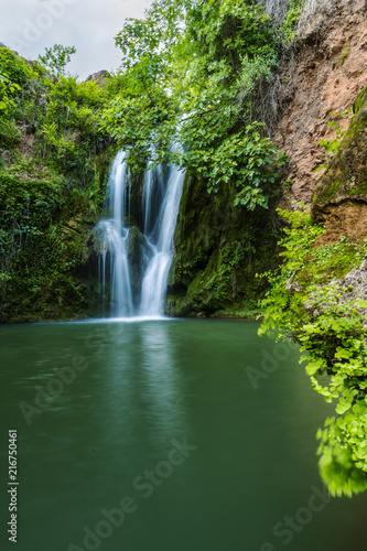 View to tall cascade falling to pond in green forest in long exposure © aitormmfoto