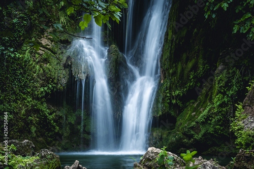 Clean cascade water flowing on rock to pond in green woods in long exposure