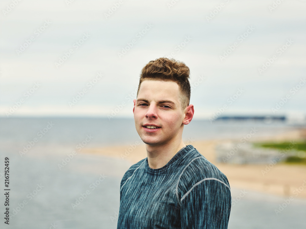 Portrait of young athlete in sportswear looking at camera while recovering from training by sea on cold day Portrait of young athlete in sportswear looking at camera while recovering from training by sea on cold day