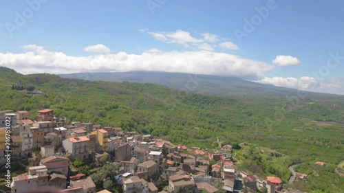 Time-lapse of the Vulcano Etna cover by clouds, view from a little village at the slope of the Volcano surrounded by a green forest with red houses photo