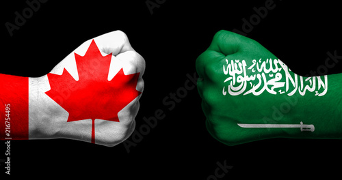 Flags of Canada and Saudi Arabia painted on two clenched fists facing each other on black background/Canada and Saudi Arabia relations concept photo