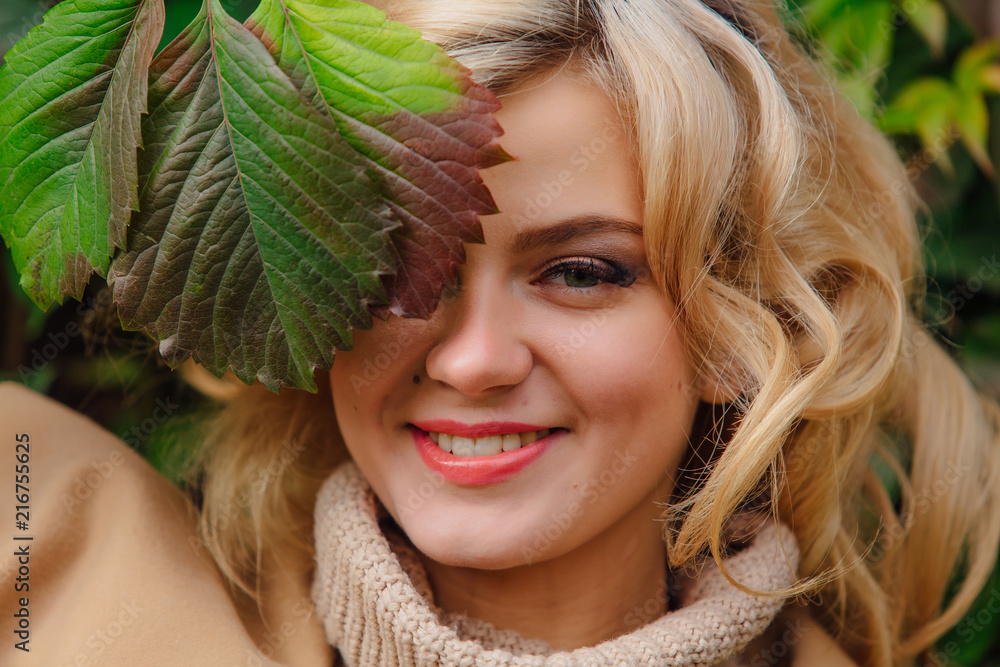 Yuong beautiful woman in sweater and coat stands next to the background of wild grapes leaves Yuong beautiful woman in sweater and coat stands next to the background of wild grapes leaves
