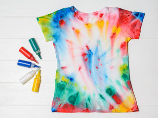 Tubes of paint for clothes and t-shirt in tie dye style on a white table. Flat lay.