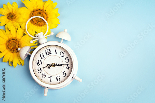 Fototapeta Naklejka Na Ścianę i Meble -  White alarm clock and yellow sunflowers on blue background.
