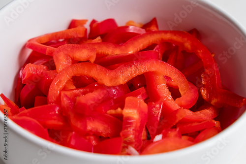 top diagonal view of sliced red bell pepper in white bowl on white counter top