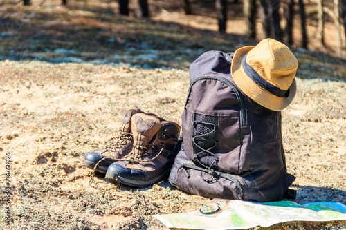 Tourist backpack with hiking boots, hat, compass and map on the glade in pine forest