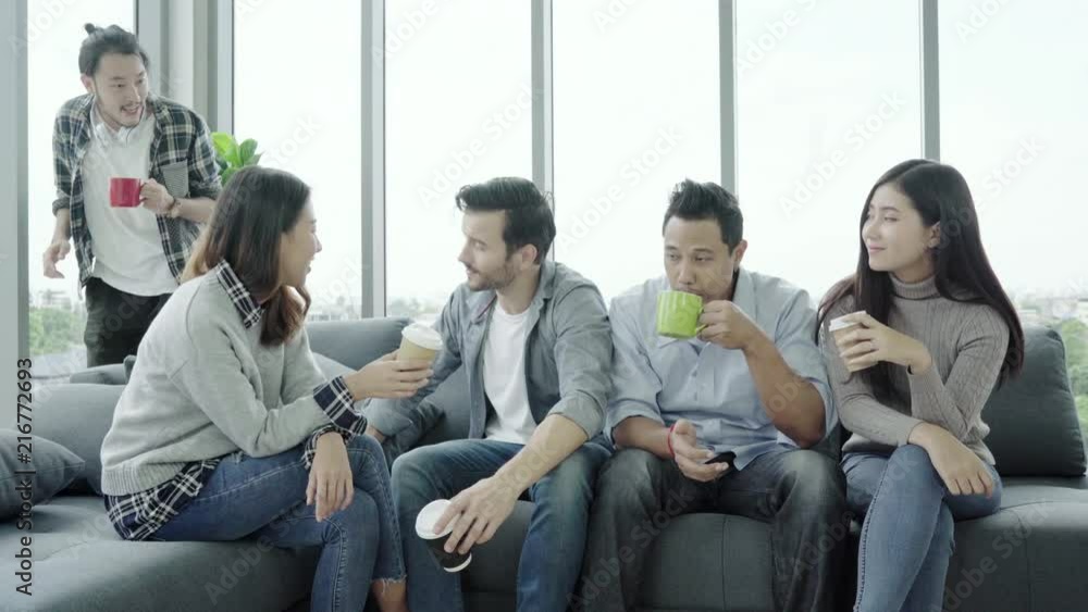 Diversity of young people group team holding coffee cups and discussing something with smile while sitting on the couch at office. Coffee break time at creative office. Diversity of young people group team holding coffee cups and discussing something with smile while sitting on the couch at office. Coffee break time at creative office.