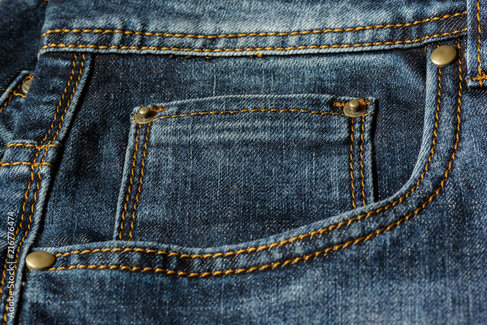 Close-up of a piece of blue jeans with orange stitches. Pocket with rivets close-up. Close-up of a piece of blue jeans with orange stitches. Pocket with rivets close-up.