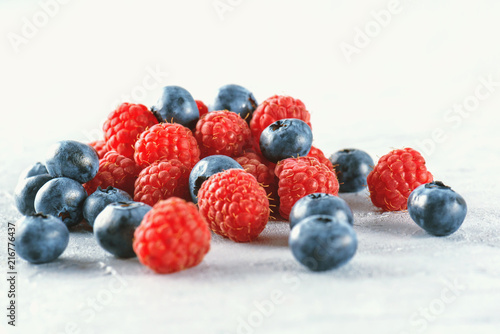 Blueberries and raspberries on the background of gray cement. Ripe and juicy fresh raspberries and blueberries close-up. A lot of berries close-up.