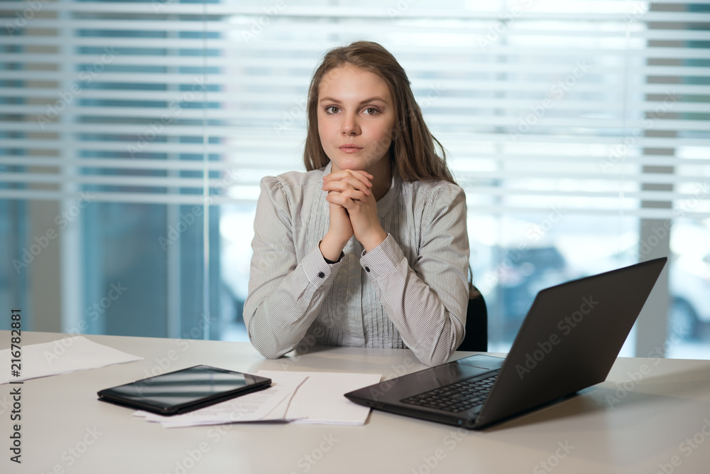 young girl businesswoman in casual clothes, sitting at a table closely look at documents, working at computer young girl businesswoman in casual clothes, sitting at a table closely look at documents, working at computer