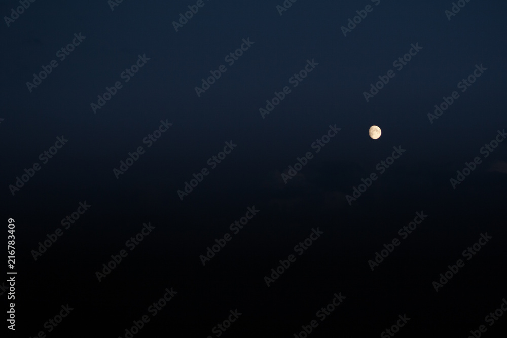 three-quarters of the growing moon on the navy blue sky background  with some visible clouds