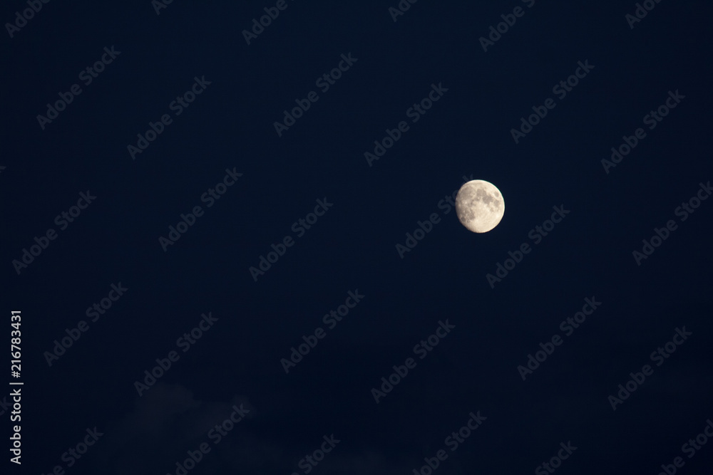 three-quarters of the growing moon in the navy blue sky with some visible clouds three-quarters of the growing moon in the navy blue sky with some visible clouds