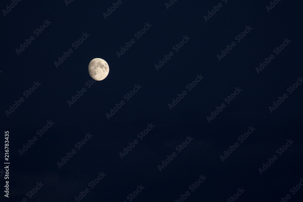 three-quarters of the growing moon in the navy blue sky with some visible clouds three-quarters of the growing moon in the navy blue sky with some visible clouds