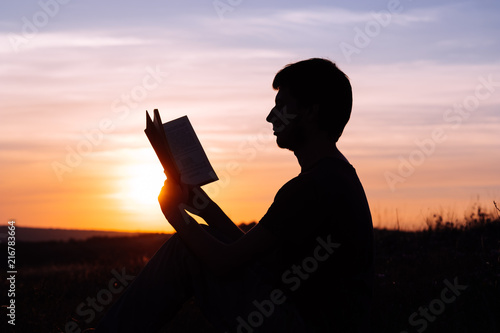 Man reading in the park against sunset.