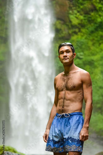 Hot man standing near waterfall. Athletic male looking happy and confident.