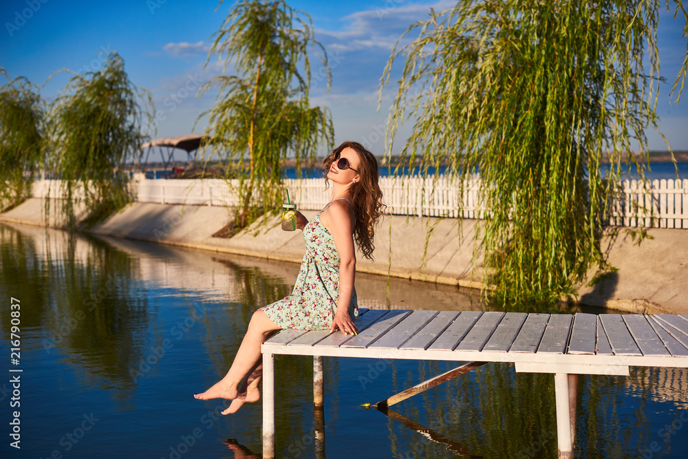 girl sitting on wooden dock over the water with my eyes closed and enjoying warm summer sunny day, side view.