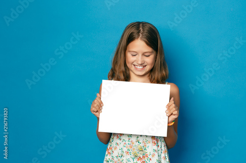 beautiful smiling child (girl) with white teeth holding in hands white blank copy space for the announcement photo
