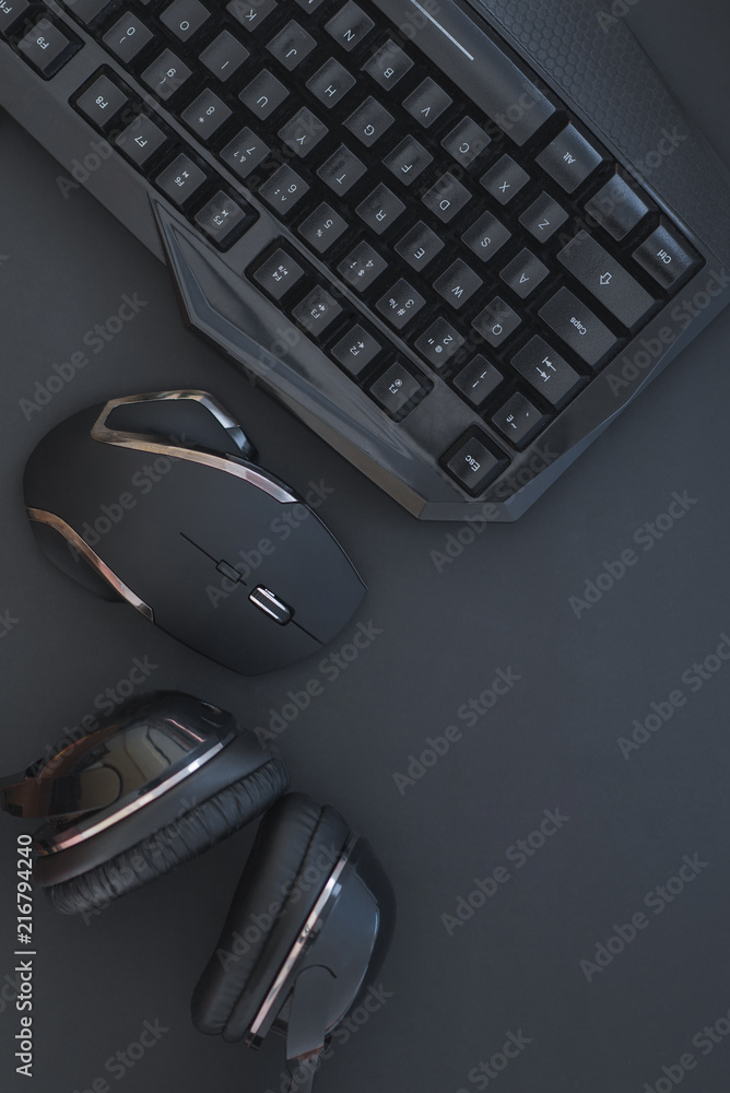 Black mouse, the keyboard, the headphones are isolated on a dark background, the top view. Flat lay gamer background. Workplace with a keyboard, mouse and headphones on a black background. Copyspace Black mouse, the keyboard, the headphones are isolated on a dark background, the top view. Flat lay gamer background. Workplace with a keyboard, mouse and headphones on a black background. Copyspace