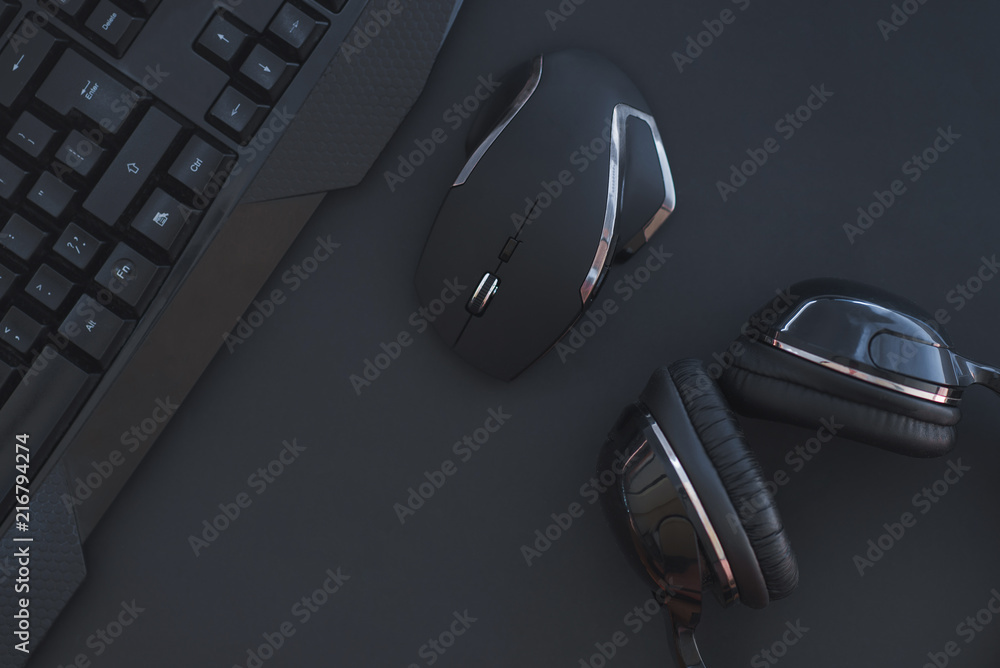 Black mouse, the keyboard, the headphones are isolated on a dark background, the top view. Flat lay gamer background. Workplace with a keyboard, mouse and headphones on a black background. Copyspace - obrazy, fototapety, plakaty 
