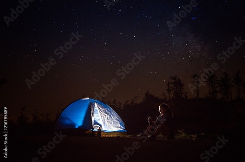 Young woman using phone on night camp on mountain trail.