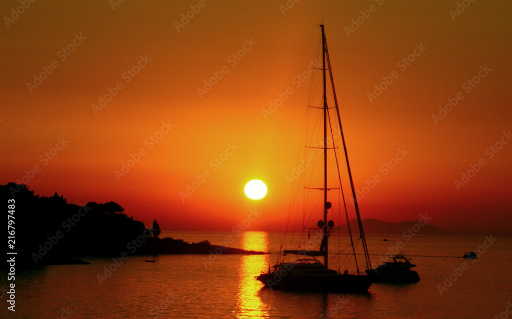 bright red and orange Sunset on sea with sailing boat with the sun on the background