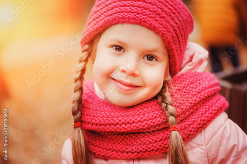 autumn close up portrait of happy little child girl enjoying the walk in sunny park in warm knitted hat and scarf