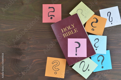 Holy bible and colorful note pads with question marks on brown wooden background as symbol for answers you can find in the bible or passages you don't understand