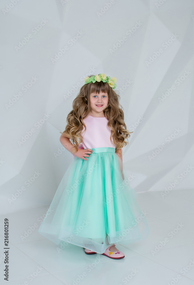 Beautiful little girl in mint dress. Girl with a wreath and flowers in a white room Beautiful little girl in mint dress. Girl with a wreath and flowers in a white room