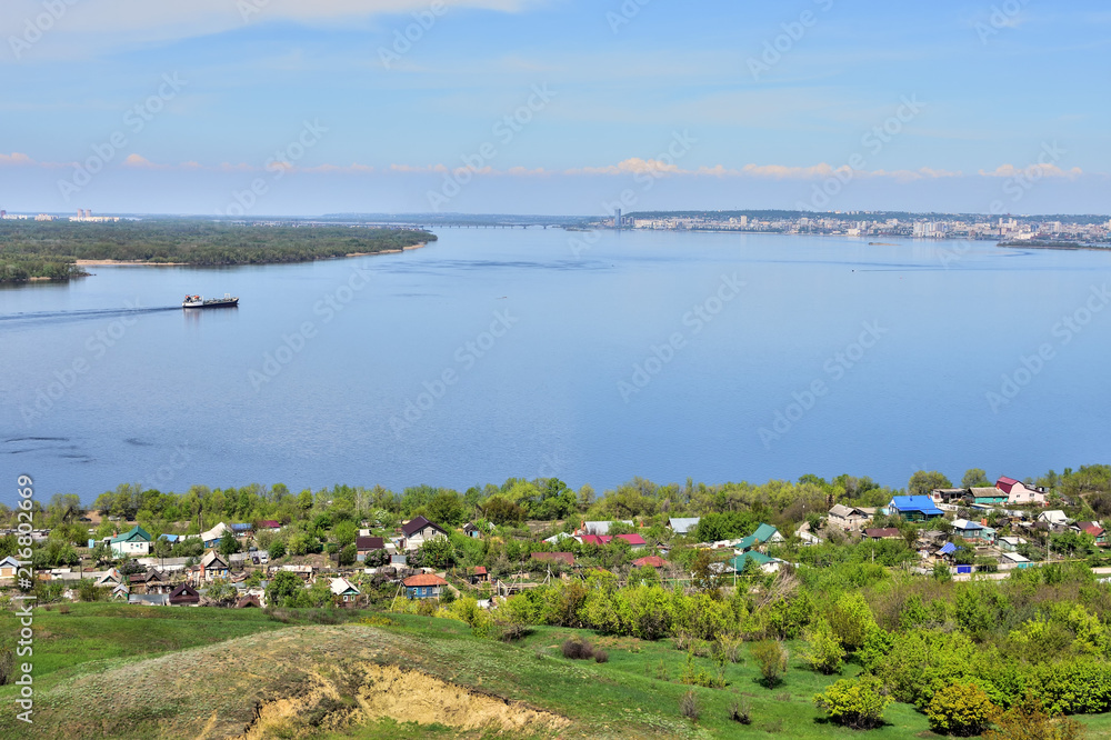 view of the bend of the Volga River from the hill, suburban and urban buildings, coastline, islands, green vegetation, tanker going along the river in the background, Saratov, Russia