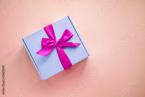 One purple paper box with bright pink ribbon bow on colored background from above. Minimalism, copy space © Iuliia