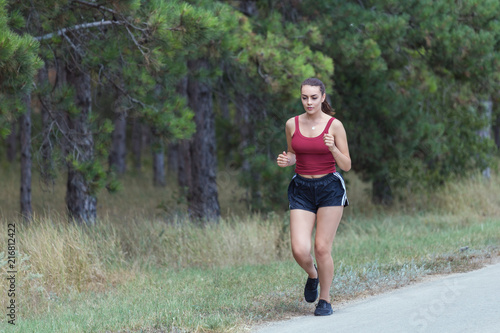 Young woman running near forest on a beautiful day. Girl running on forest trail to lose weight and maintain a healthy life.