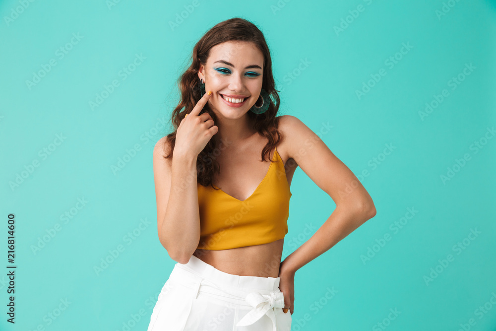 Image of glamour fashionable woman 20s with beautiful makeup smiling and pointing finger on cheek, isolated over blue background Image of glamour fashionable woman 20s with beautiful makeup smiling and pointing finger on cheek, isolated over blue background
